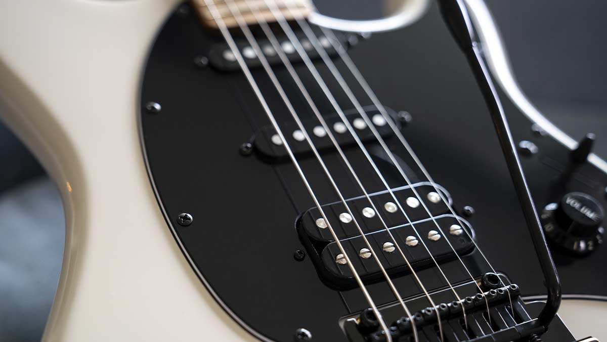 Closeup of an electric guitar with black pickguard and single coil pickups