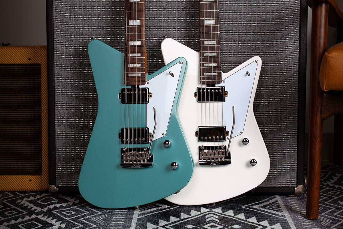 Mariposa guitars in Dorado Green and Imperial White resting against an amp. 